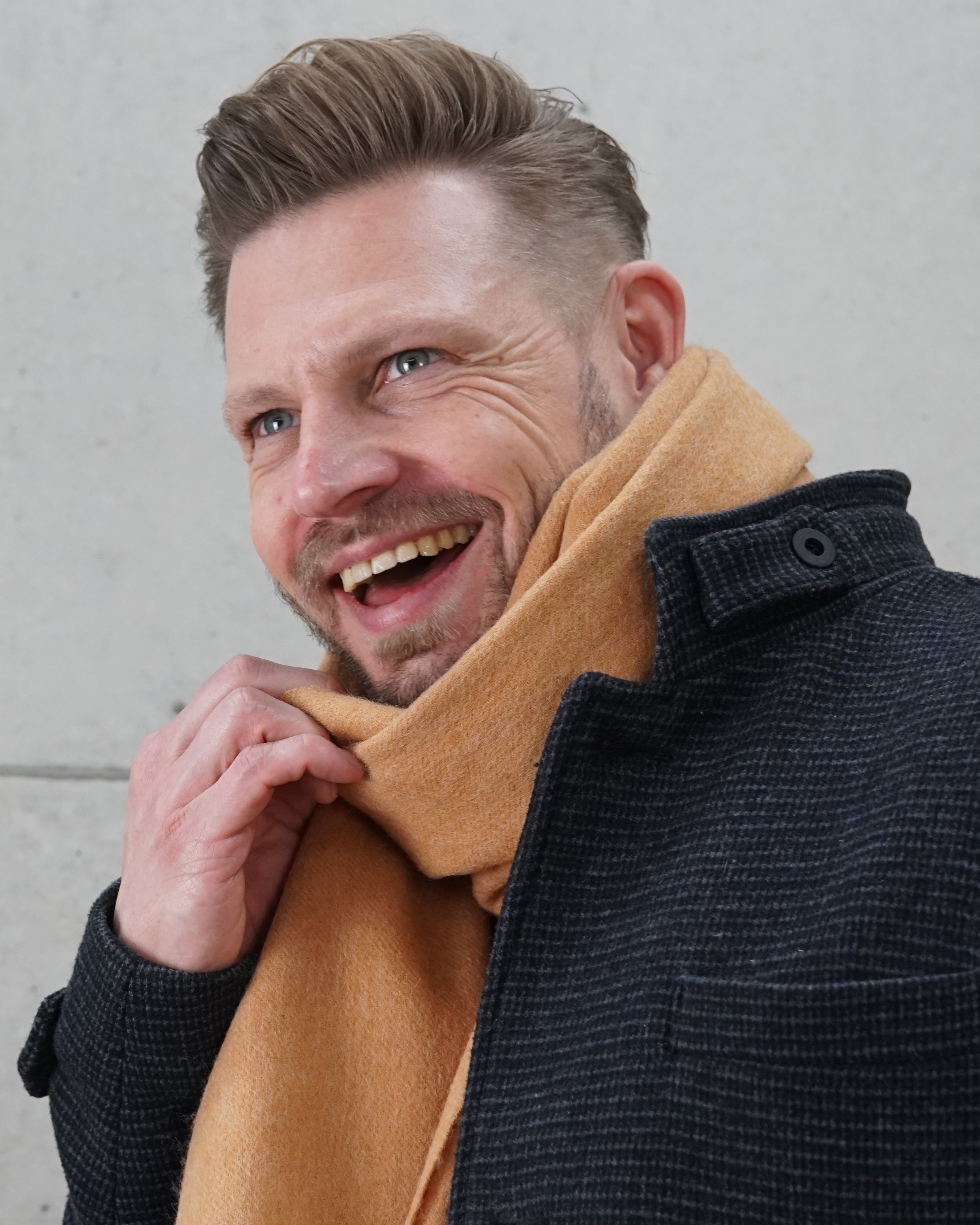 Schal „Caramel Warmth“ aus 100% karamellfarbener Schurwolle getragen von einem Mann in dunkler Jacke